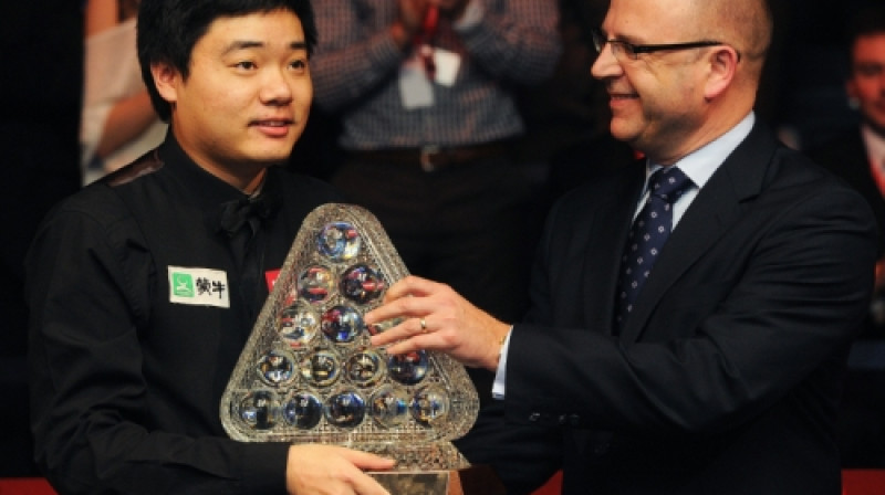 Dings Junhui saņem "Masters" trofeju no turnīra galvenā sponsora "Ladbrokes" pārstāvja Gerija Makilraita rokām.
Foto: AFP/Scanpix